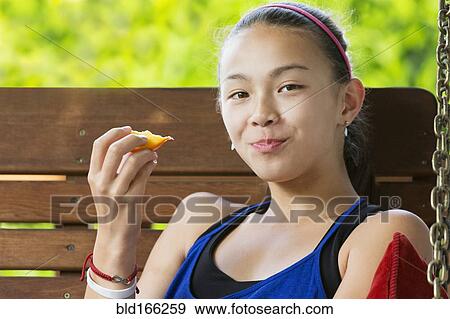 Stock Photo - Mixed race girl eating fruit on porch swing. Fotosearch