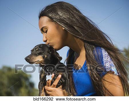 Stock Image - Mixed race girl kissing dog outdoors. Fotosearch