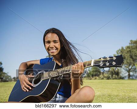 Stock Photo - Mixed race girl playing guitar in park. Fotosearch