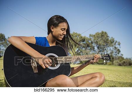 Stock Photography - Mixed race girl playing guitar in park. Fotosearch