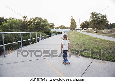 Stock Photo - Mixed race girl riding skateboard in park. Fotosearch