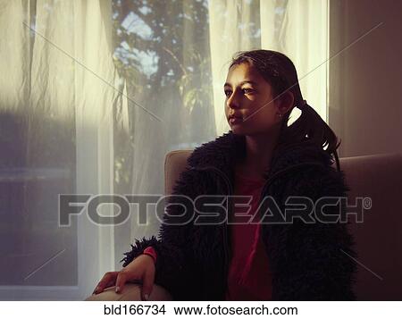 Picture - Mixed race girl sitting on sofa in living room. Fotosearch