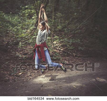 Picture - Mixed race girl swinging from tree branch on dirt path. Fotosearch
