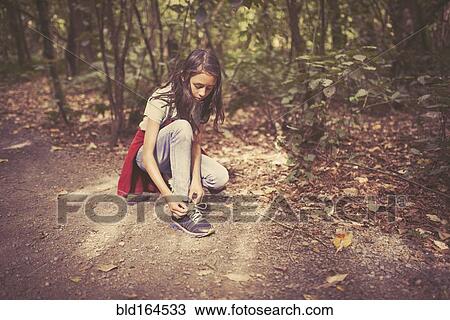 Stock Image - Mixed race girl tying shoelaces on dirt path. Fotosearch