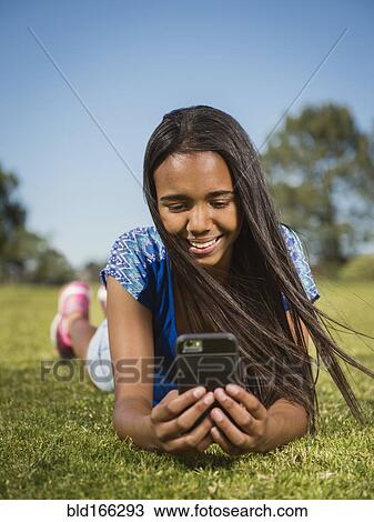 Stock Image - Mixed race girl using cell phone in park. Fotosearch