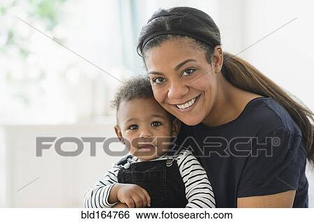 Stock Photograph - Mixed race mother holding baby son in living room. Fotosearch