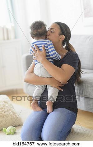 Mixed race mother kissing baby son in living room View Large Photo Image Stock Photo - Mixed race mother kissing baby son in living room. Fotosearch