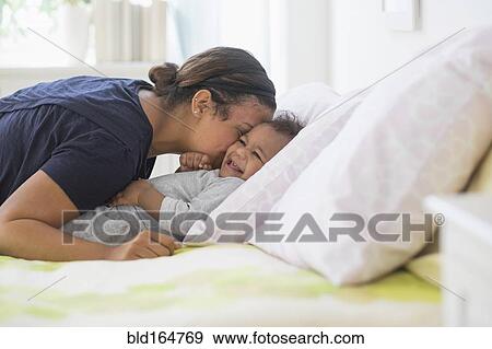 Stock Photo - Mixed race mother kissing baby son on bed. Fotosearch