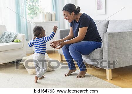 Stock Image - Mixed race mother playing with baby son in living room. Fotosearch