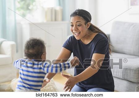 Stock Image - Mixed race mother playing with baby son in living room. Fotosearch