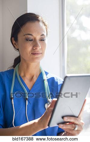 Stock Photo - Mixed race nurse using digital tablet at window. Fotosearch