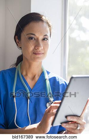 Mixed race nurse using digital tablet at window View Large Photo Image Stock Photo - Mixed race nurse using digital tablet at window. Fotosearch