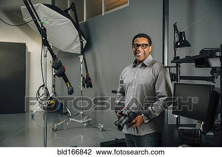 Stock Image - Mixed race photographer holding camera in studio. Fotosearch
