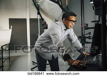 Stock Image - Mixed race photographer using computer in studio. Fotosearch