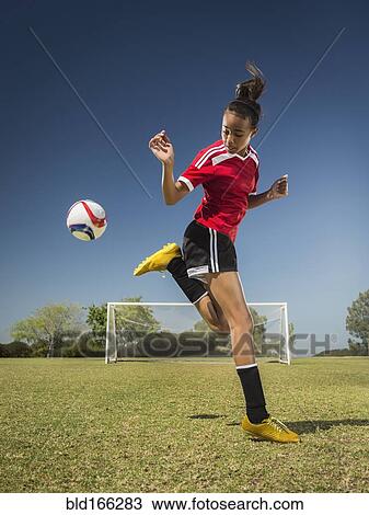 Stock Image - Mixed race soccer player kicking ball on field. Fotosearch