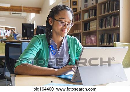 Stock Image - Mixed race student using digital tablet in library. Fotosearch