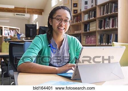 Stock Image - Mixed race student using digital tablet in library. Fotosearch