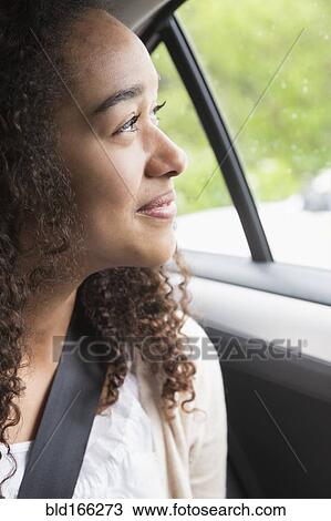 Stock Image - Mixed race teenage girl smiling in car back seat. Fotosearch