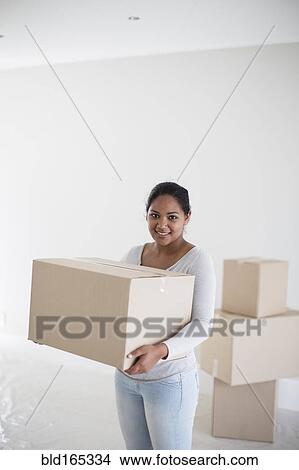 Picture - Mixed race woman carrying cardboard box in new home. Fotosearch