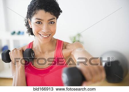 Stock Image - Mixed race woman lifting weights in gym. Fotosearch