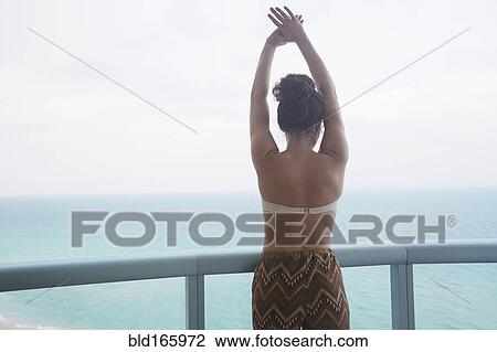 Stock Image - Mixed race woman overlooking ocean from balcony. Fotosearch