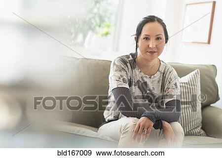 Stock Photo - Mixed race woman sitting on sofa in living room. Fotosearch