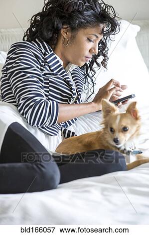 Mixed race woman using cell phone with dog on bed View Large Photo Image Stock Photo - Mixed race woman using cell phone with dog on bed. Fotosearch