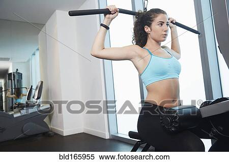 Stock Photography - Mixed race woman using exercise machine in gym. Fotosearch