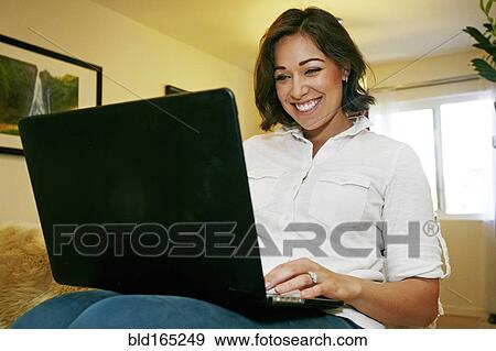 Stock Photo - Mixed race woman using laptop on sofa. Fotosearch