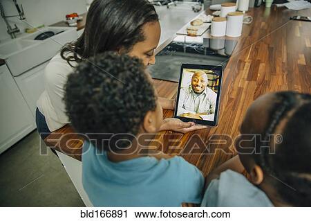 Stock Image - Mother and children video chatting with father in kitchen. Fotosearch