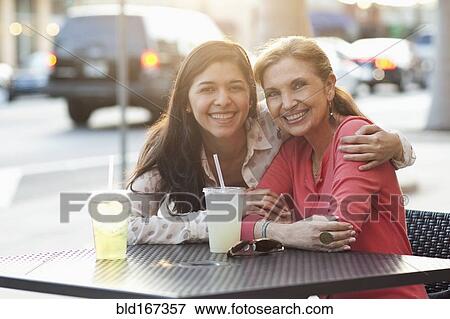 Stock Photo - Mother and daughter hugging at sidewalk cafe. Fotosearch