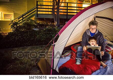 Stock Photograph - Mother and son using digital tablet in backyard tent. Fotosearch