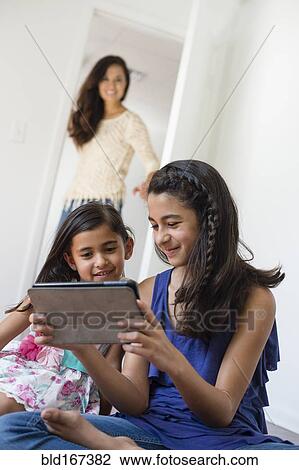 Stock Image - Mother watching daughters use digital tablet. Fotosearch