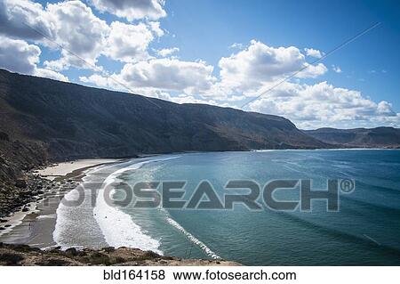 Stock Photo - Ocean waves on beach under mountains. Fotosearch