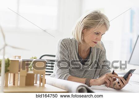 Stock Image - Older Caucasian architect using cell phone in office. Fotosearch