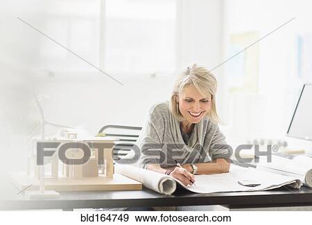 Stock Photo - Older Caucasian architect writing on blueprints in office. Fotosearch