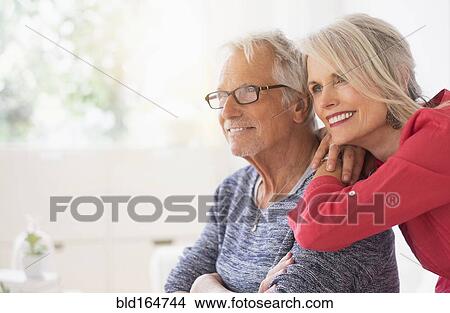 Picture - Older Caucasian couple hugging in living room. Fotosearch