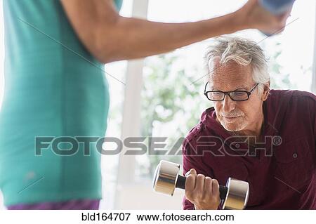 Stock Photo - Older Caucasian couple lifting weights in gym. Fotosearch