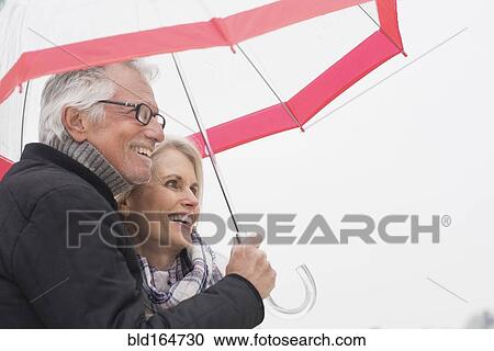 Stock Image - Older Caucasian couple standing under umbrella. Fotosearch