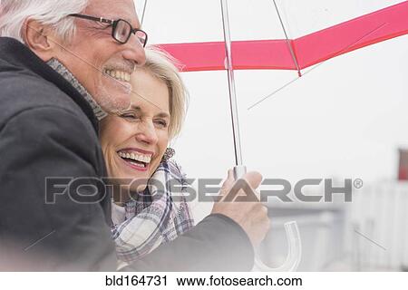 Stock Image - Older Caucasian couple standing under umbrella. Fotosearch