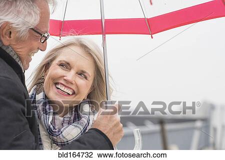Stock Image - Older Caucasian couple standing under umbrella. Fotosearch