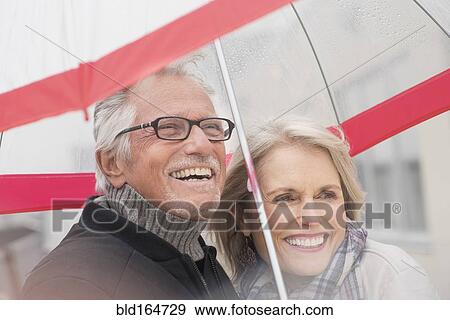 Stock Photo - Older Caucasian couple standing under umbrella. Fotosearch