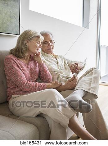 Stock Image - Older Caucasian couple using digital tablet on sofa. Fotosearch
