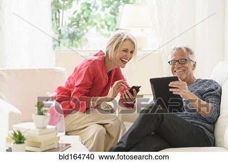 Stock Image - Older Caucasian couple using technology in living room. Fotosearch