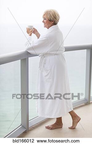 Stock Image - Older Caucasian woman drinking coffee on balcony. Fotosearch
