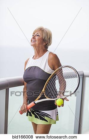 Older Caucasian woman holding tennis racket on balcony View Large Photo Image Stock Photo - Older Caucasian woman holding tennis racket on balcony. Fotosearch