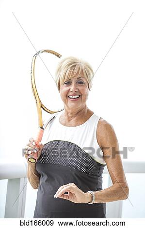Stock Photo - Older Caucasian woman holding tennis racket on balcony. Fotosearch