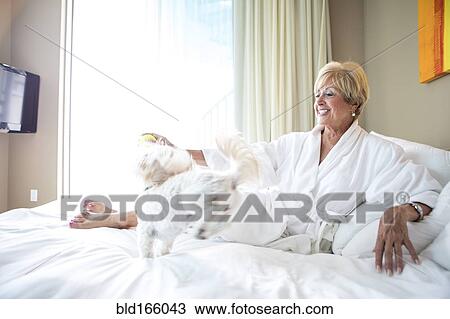 Stock Image - Older Caucasian woman petting dog on bed. Fotosearch