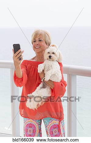 Stock Photo - Older Caucasian woman taking selfie with dog on balcony. Fotosearch