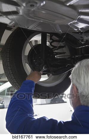 Stock Image - Older Hispanic mechanic repairing car in garage. Fotosearch
